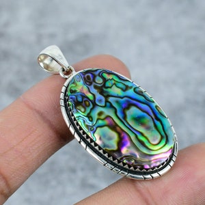 May include: An oval-shaped pendant with a silver setting and a colorful abalone shell inlay. The shell has iridescent green, blue, and purple hues.