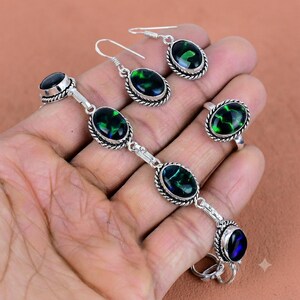 May include: A jewellery set consisting of a bracelet, a ring, and a pair of earrings. Each piece features oval-shaped black stones with iridescent green and blue flecks, set in silver-toned metal with a twisted rope-style border detail.