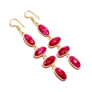 Può includere: Un paio di orecchini pendenti color oro con più pietre preziose rosa brillante, ovali e sfaccettate. Gli orecchini hanno una chiusura a gancio. Le pietre sono disposte a cascata su sfondo bianco.