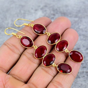 May include: A pair of long, dangling earrings with multiple oval-shaped red gemstones. The earrings are made of gold-toned metal.