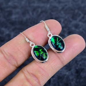 Peut inclure: Une paire de boucles d'oreilles en argent avec des pierres précieuses ovales noires et vertes. Les pierres présentent un motif tourbillonnant vert vif sur un fond sombre. Les boucles sont présentées sur un fond neutre.