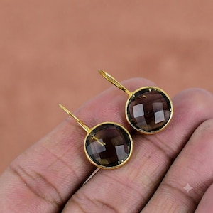 May include: A pair of round earrings featuring faceted, translucent dark brown smoky quartz gemstones set in gold-toned metal bezels with matching gold-toned ear wires. The stones have a geometric, multi-faceted cut that reflects light.