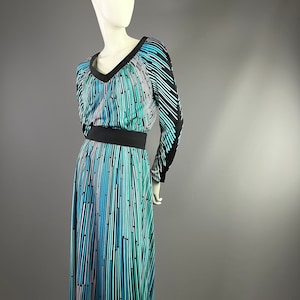 Peut inclure: Une longue robe &agrave; motif noir et bleu avec un col en V et des manches longues. La robe a une ceinture noire et une jupe fluide.