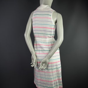 May include: A white sleeveless dress with horizontal stripes in pink, green, and purple. The dress has a collared neckline and a drawstring waist.