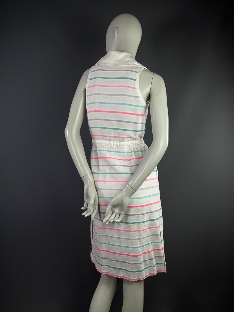 May include: A white sleeveless dress with horizontal stripes in pink, green, and purple. The dress has a collared neckline and a drawstring waist.