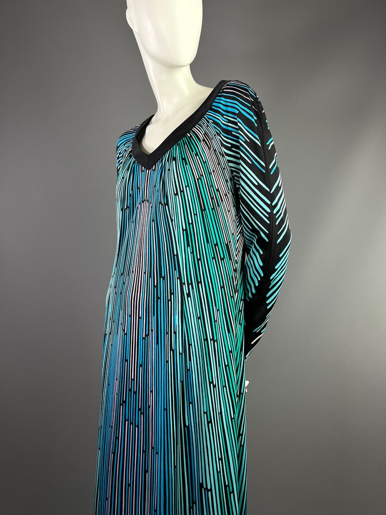 Peut inclure: Une robe &agrave; manches longues avec un col en V et un motif g&eacute;om&eacute;trique de rayures verticales dans des tons de bleu, vert et noir.