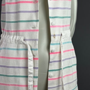 May include: A white sleeveless dress with pink, purple, and green stripes. The dress has a white drawstring waist and white buttons down the front.