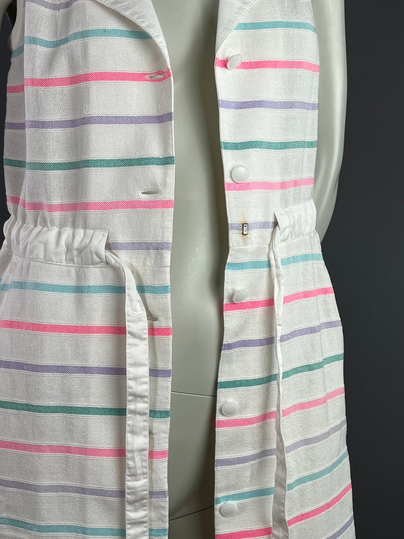 May include: A white sleeveless dress with pink, purple, and green stripes. The dress has a white drawstring waist and white buttons down the front.