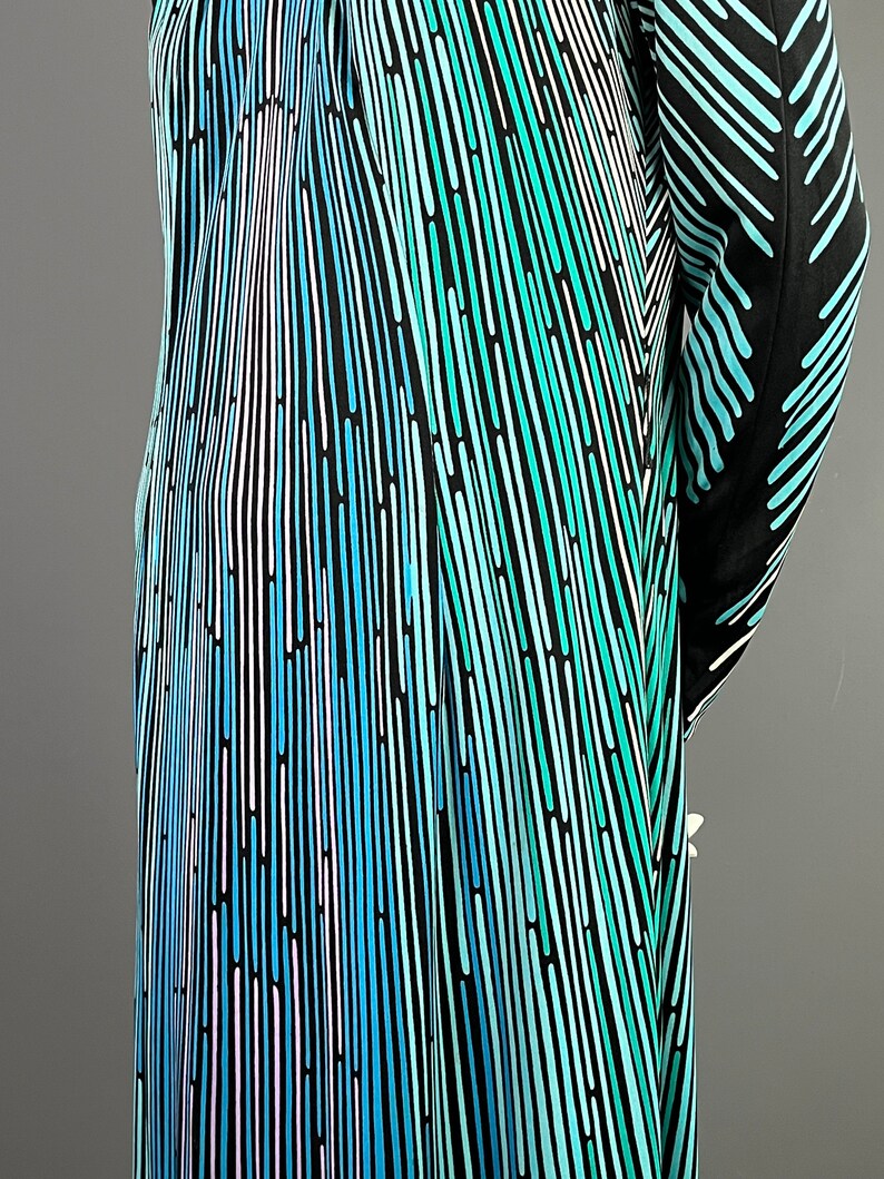 Peut inclure: Une robe noire avec un motif abstrait bleu, vert et blanc. Le motif est compos&eacute; de fines lignes qui cr&eacute;ent un effet ray&eacute;.