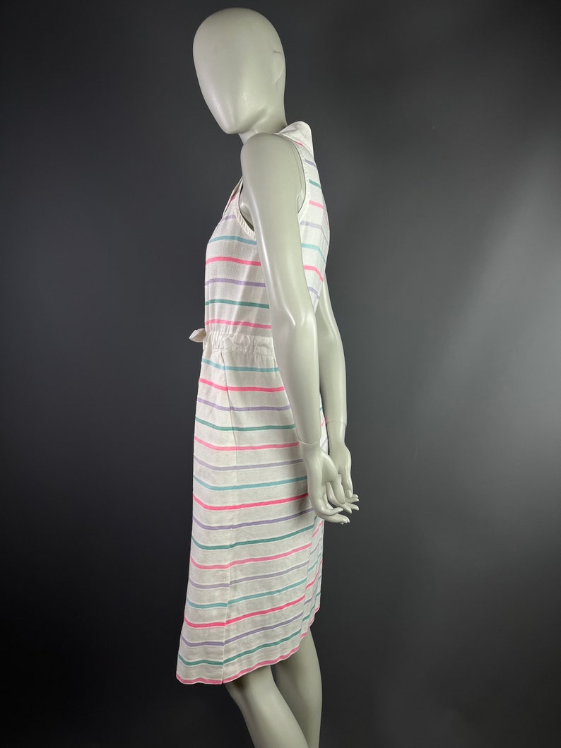 May include: A white sleeveless dress with horizontal stripes in pink, green, and purple. The dress has a drawstring waist and a collared neckline.