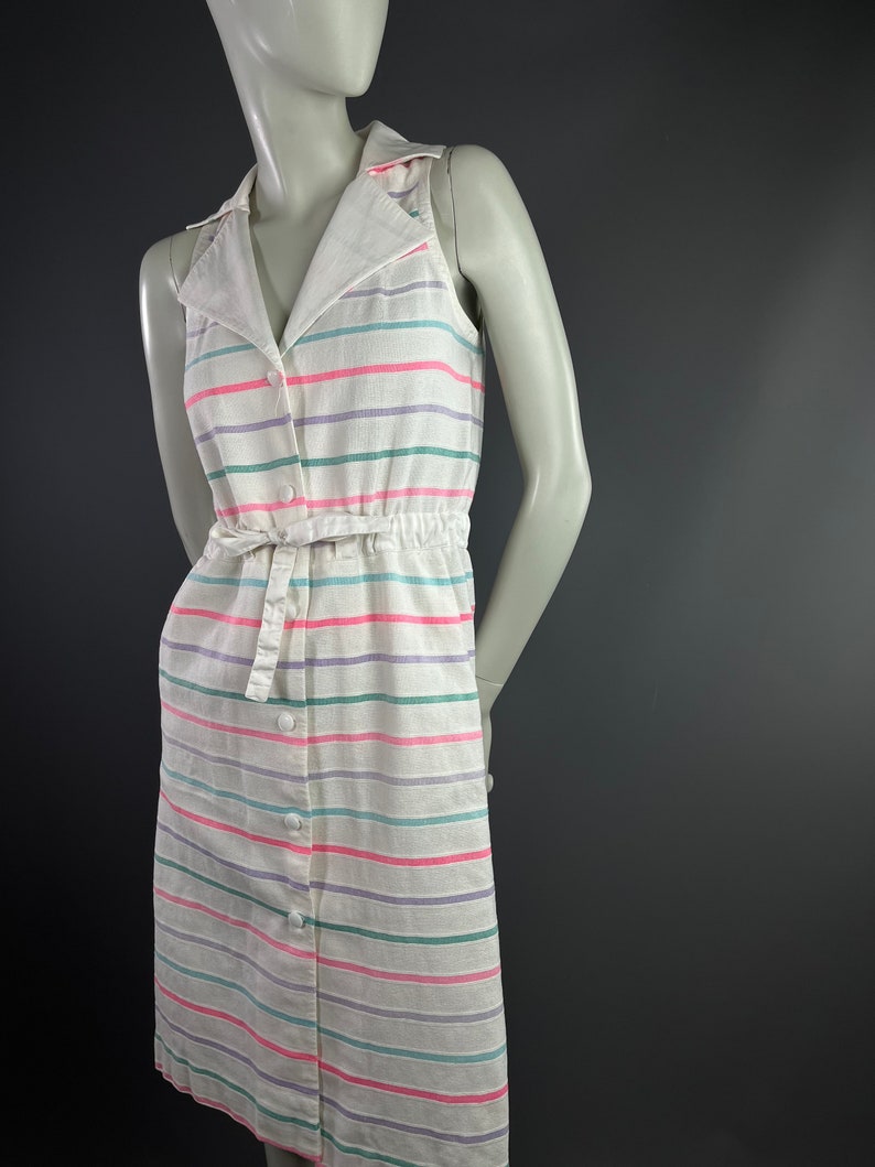 May include: A white sleeveless dress with a collared neckline and a button-up front. The dress has a striped pattern in pink, green, and purple.