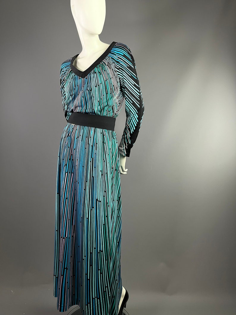 Peut inclure: Une longue robe &agrave; motif noir et bleu avec un col en V et des manches longues. La robe a une ceinture noire et une jupe fluide.