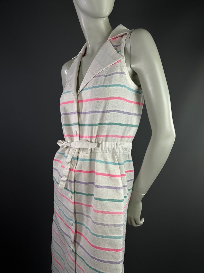 May include: A white sleeveless dress with a striped pattern in pink, green, and purple. The dress has a collared neckline, a button-up front, and a tie belt at the waist.
