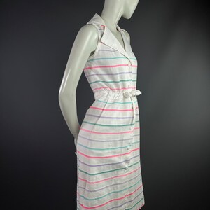 May include: A white sleeveless dress with a collared neckline and a button-up front. The dress has a striped pattern in pink, green, and purple.