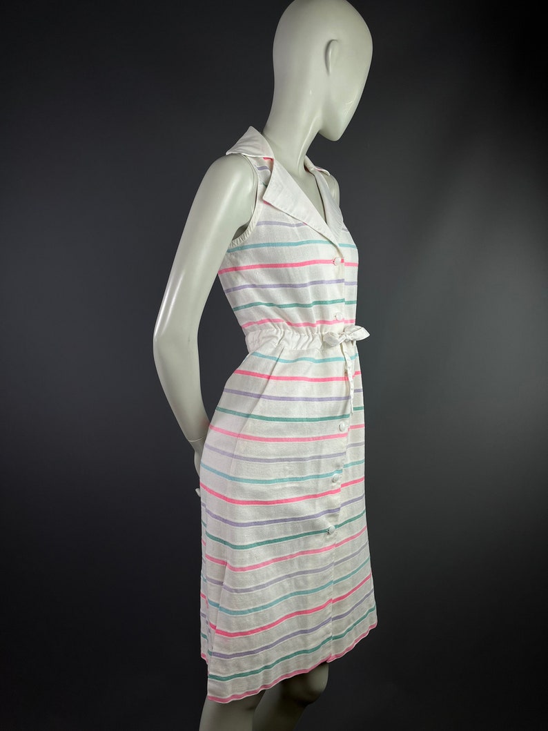 May include: A white sleeveless dress with a collared neckline and a button-up front. The dress has a striped pattern in pink, green, and purple.