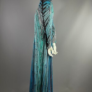 Peut inclure: Une longue robe maxi fluide avec un motif g&eacute;om&eacute;trique dans les tons de bleu, vert et noir. La robe a un col en V et des manches longues.