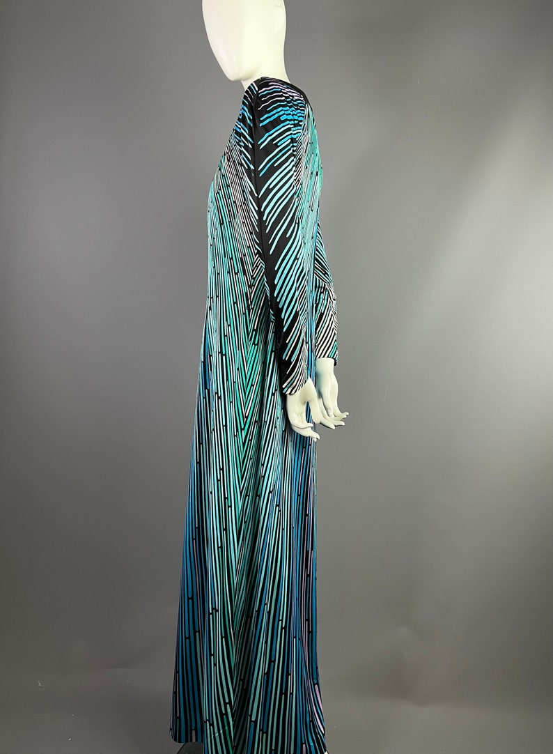 Peut inclure: Une longue robe maxi fluide avec un motif g&eacute;om&eacute;trique dans les tons de bleu, vert et noir. La robe a un col en V et des manches longues.