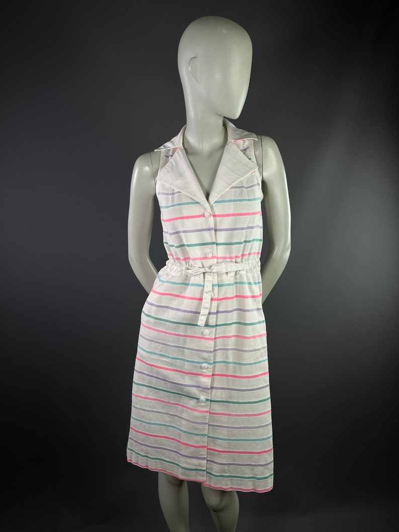 May include: A white sleeveless dress with a striped pattern in pink, green, and purple. The dress has a collared neckline, button closure, and a tie at the waist.