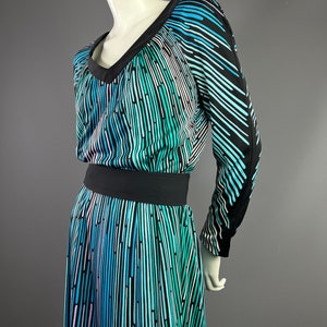 Peut inclure: Une robe &agrave; manches longues avec un fond noir et un motif abstrait color&eacute; de lignes verticales dans des tons de bleu, vert et rose. La robe a un col en V et une ceinture noire.