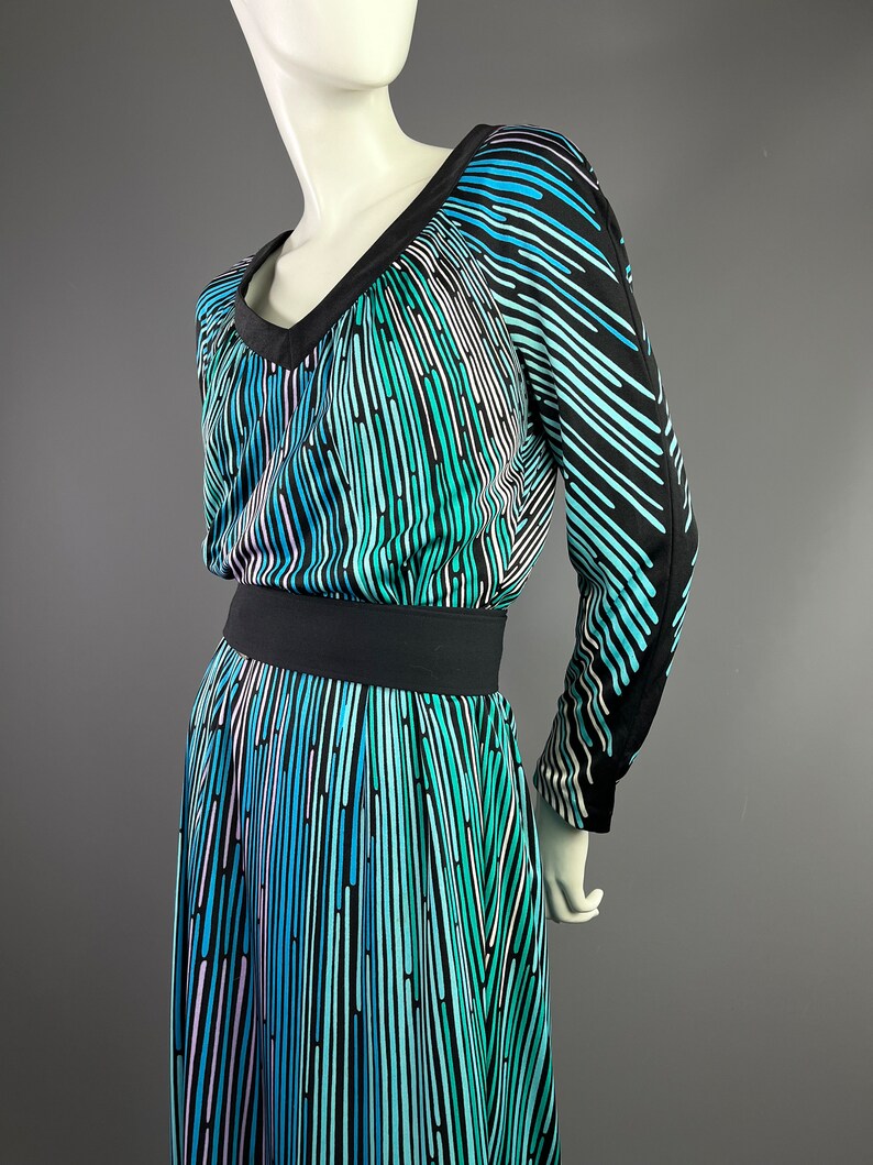 Peut inclure: Une robe &agrave; manches longues avec un fond noir et un motif abstrait color&eacute; de lignes verticales dans des tons de bleu, vert et rose. La robe a un col en V et une ceinture noire.