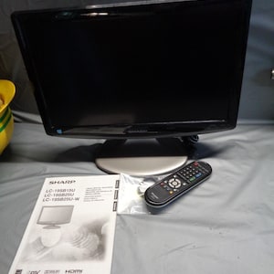 May include: A black Sharp LCD television with a silver base, accompanied by a black remote control and an operation manual labeled with model numbers LC-19SB15U, LC-19SB25U, and LC-19SB25U-W, featuring DTV, Dolby Digital, and HDMI logos.