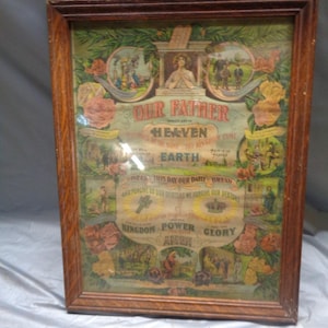 May include: A rectangular wooden frame containing a vintage religious print featuring the Lord's Prayer. The artwork includes floral borders, small illustrative scenes, and central text reading Our Father, Heaven, Earth, Kingdom, Power, and Glory.