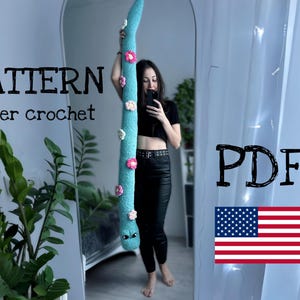 Puede incluir: Un patrón de crochet para una serpiente larga y azul con flores rosas. El patrón está disponible para descargar en PDF. El texto "PATTERN finger crochet PDF" es visible en la imagen.