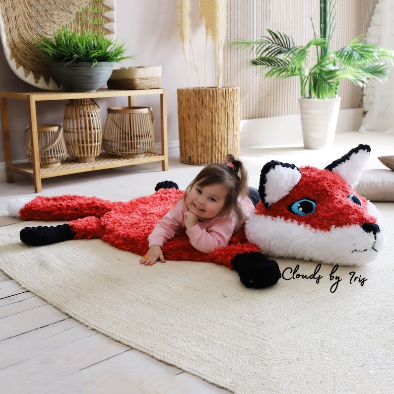 May include: A red and white crocheted fox rug with black feet and a girl lying on it. The rug has a fluffy texture and the fox has large, blue eyes. The text "Clouds by Tris" is visible in the lower right corner of the image.