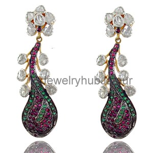 May include: A pair of ornate drop earrings. Each earring features a floral cluster at the top, connected to a teardrop-shaped design. The teardrop is filled with red and green gemstones, with a dark metal outline and clear stones.