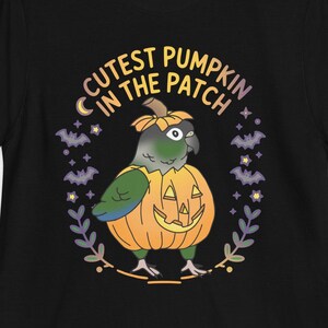 May include: Black t-shirt featuring a green and blue parrot inside an orange pumpkin with a carved face. The text "Cutest Pumpkin in the Patch" is in a circular design around the parrot. The design includes bats and leaves.