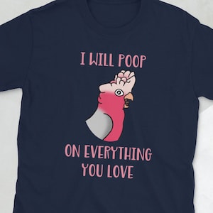 May include: Navy blue t-shirt with a pink and white cartoon parrot illustration and the text "I WILL POOP ON EVERYTHING YOU LOVE" in pink. The shirt is made of a soft material.
