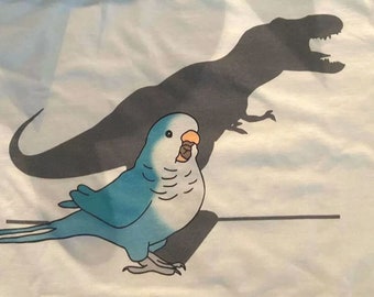 May include: A blue and gray parakeet with a shadow of a dinosaur behind it. The parakeet is facing the right side of the image. The dinosaur shadow is facing the left side of the image.