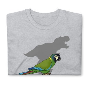 Puede incluir: Una camiseta gris con un loro verde y azul con la sombra de un Tyrannosaurus Rex detrás.