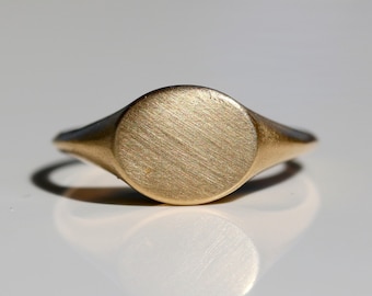 May include: A gold signet ring with a smooth, oval-shaped top.