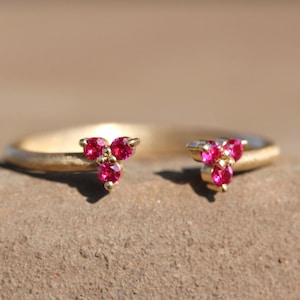 May include: A gold ring with two triangular clusters of three ruby red gemstones each.