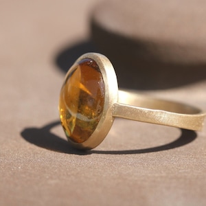 May include: A gold ring with a large, oval-shaped amber gemstone set in a bezel setting.