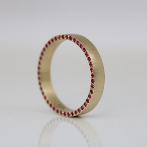 Könnte beinhalten: Ein Goldring mit einer Reihe kleiner roter Edelsteine ​​am Rand.