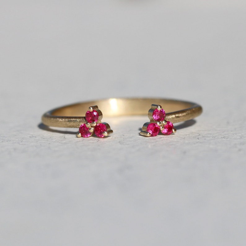 May include: A gold ring with two clusters of three pink gemstones each. The ring is open on one side, making it adjustable.