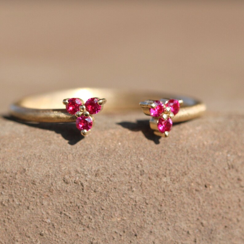 May include: A gold ring with two triangular clusters of three ruby red gemstones each.