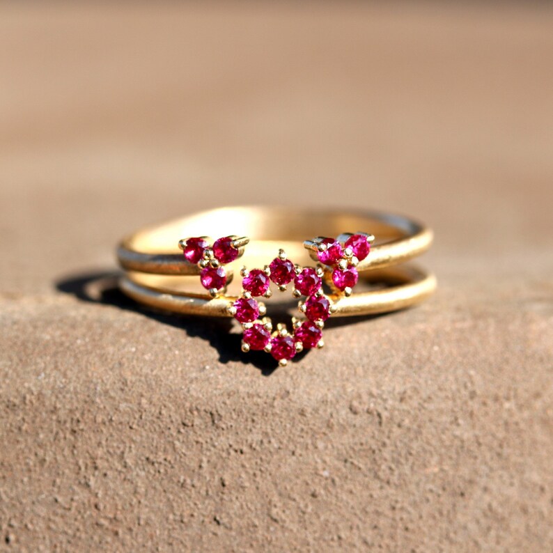 May include: A gold ring with a double band and a heart-shaped design made of small red gemstones.