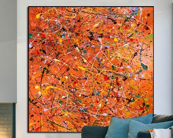 May include: Abstract painting with orange, yellow, white, and black paint splatters and lines on a canvas. The painting is hanging on a wall in a living room with a couch and a coffee table.