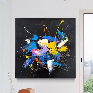 Abstract painting with splashes of blue, yellow, pink, and white paint on a black background.