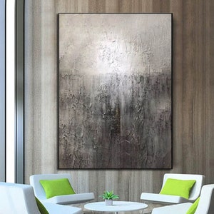May include: Abstract painting with a textured, gray and white color scheme. The painting is framed and hanging on a wall in a modern living room setting.