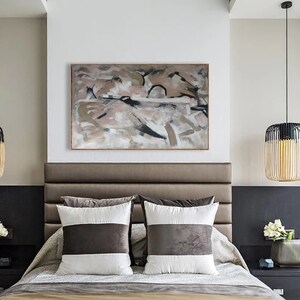 May include: A bedroom with a brown leather headboard and two white and brown striped pillows. A large abstract painting in shades of brown, pink, and black hangs above the headboard. A wooden lamp with a black shade hangs from the ceiling.