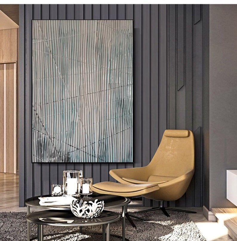 May include: Abstract art print with a blue and white striped pattern. The print is framed and hanging on a gray wall in a modern living room.