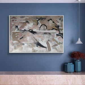 May include: Abstract painting with a white background and brown, black, and pink brushstrokes. The painting is framed in a white frame and is hanging on a blue wall.