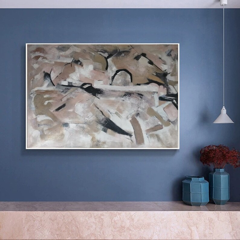 May include: Abstract painting with a white background and brown, black, and pink brushstrokes. The painting is framed in a white frame and is hanging on a blue wall.