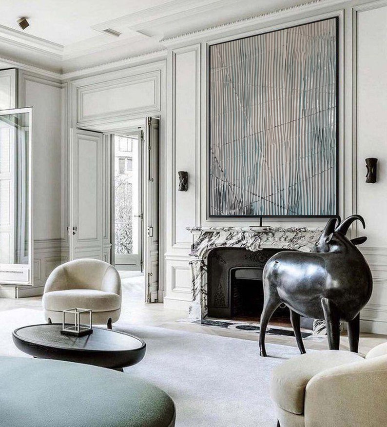 May include: A modern living room interior with a white fireplace and a black and white abstract painting above it. A black metal sculpture of a goat stands in front of the fireplace. A white armchair and a round coffee table are in the foreground.