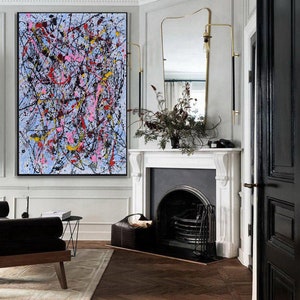 Puede incluir: Pintura abstracta con salpicaduras de pintura negra, blanca, rosa, amarilla y azul sobre un fondo azul claro. La pintura est&aacute; colgada en una pared blanca en una habitaci&oacute;n con una chimenea y una puerta negra.