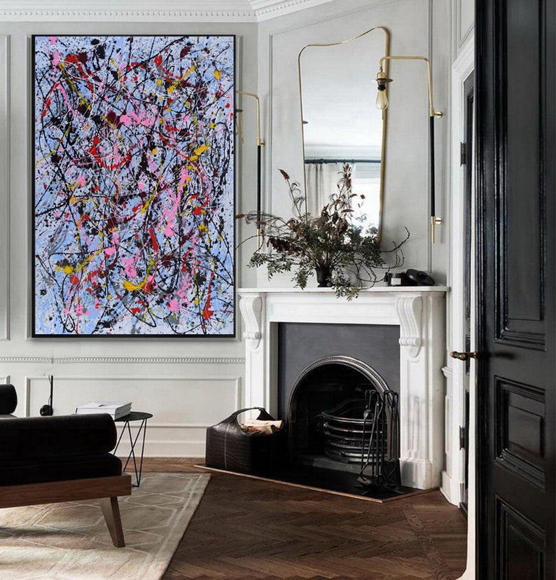 Puede incluir: Pintura abstracta con salpicaduras de pintura negra, blanca, rosa, amarilla y azul sobre un fondo azul claro. La pintura est&aacute; colgada en una pared blanca en una habitaci&oacute;n con una chimenea y una puerta negra.